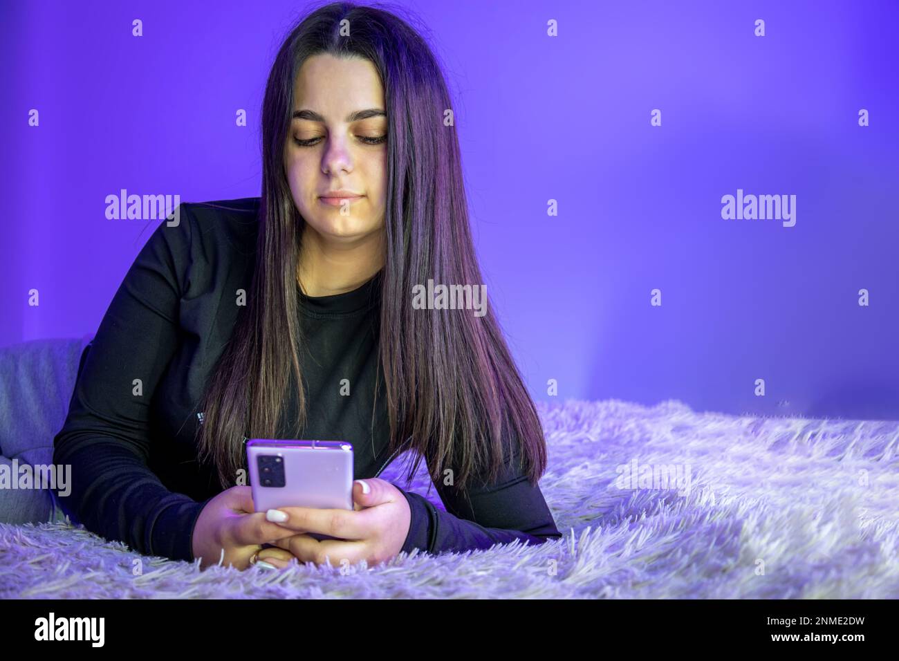 Una bella ragazza è sdraiata sul letto con un telefono cellulare. Foto Stock