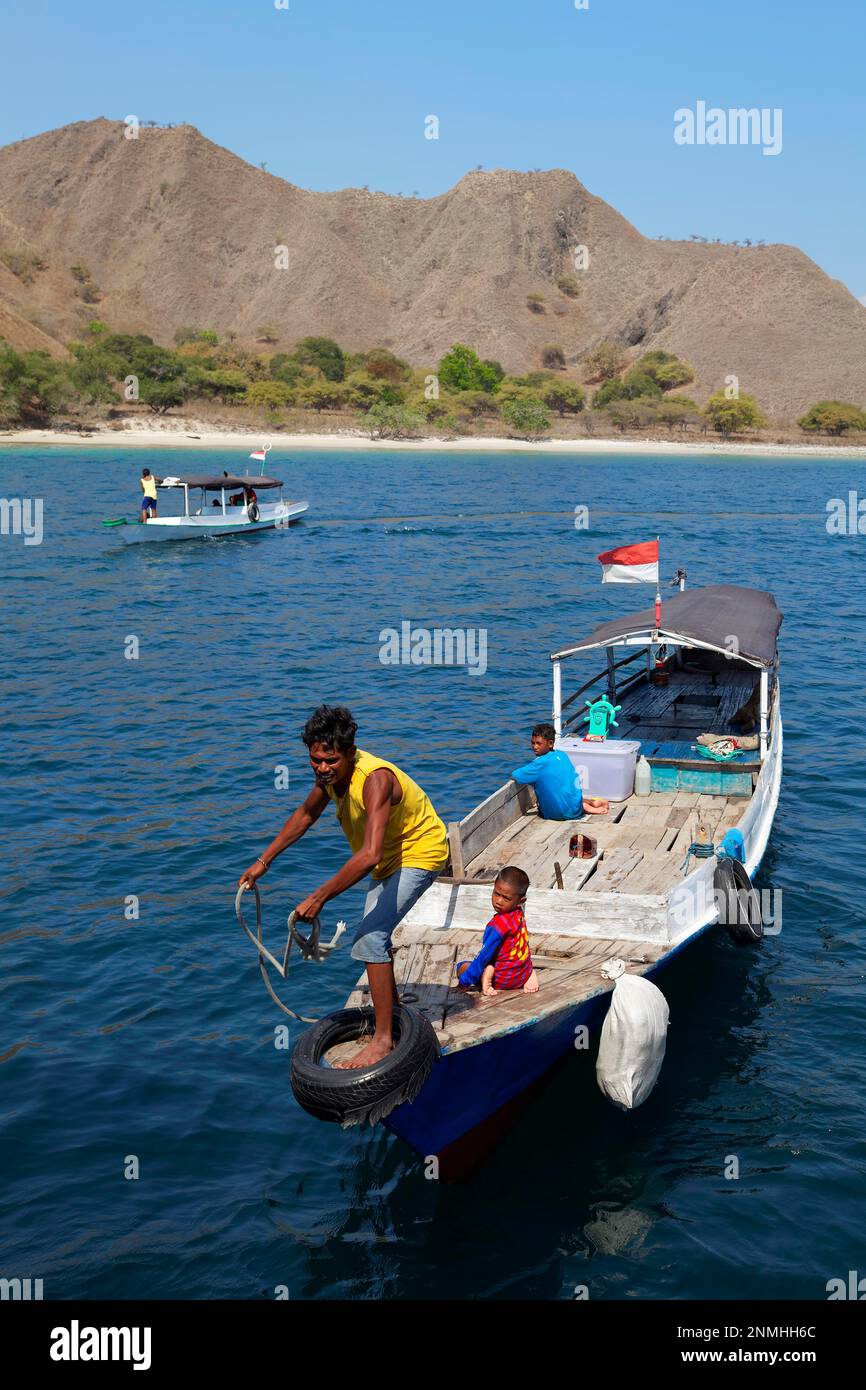 Uomo in barca da pesca in mare con i bambini, due, indonesiano, getta corda per ormeggiare, vuole vendere pesce, dietro barca di fronte al paesaggio dell'isola con Foto Stock