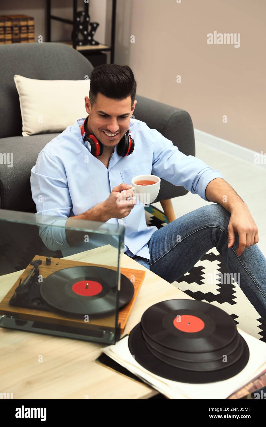 Un uomo felice beve il tè mentre ascolta la musica con il giradischi a casa Foto Stock