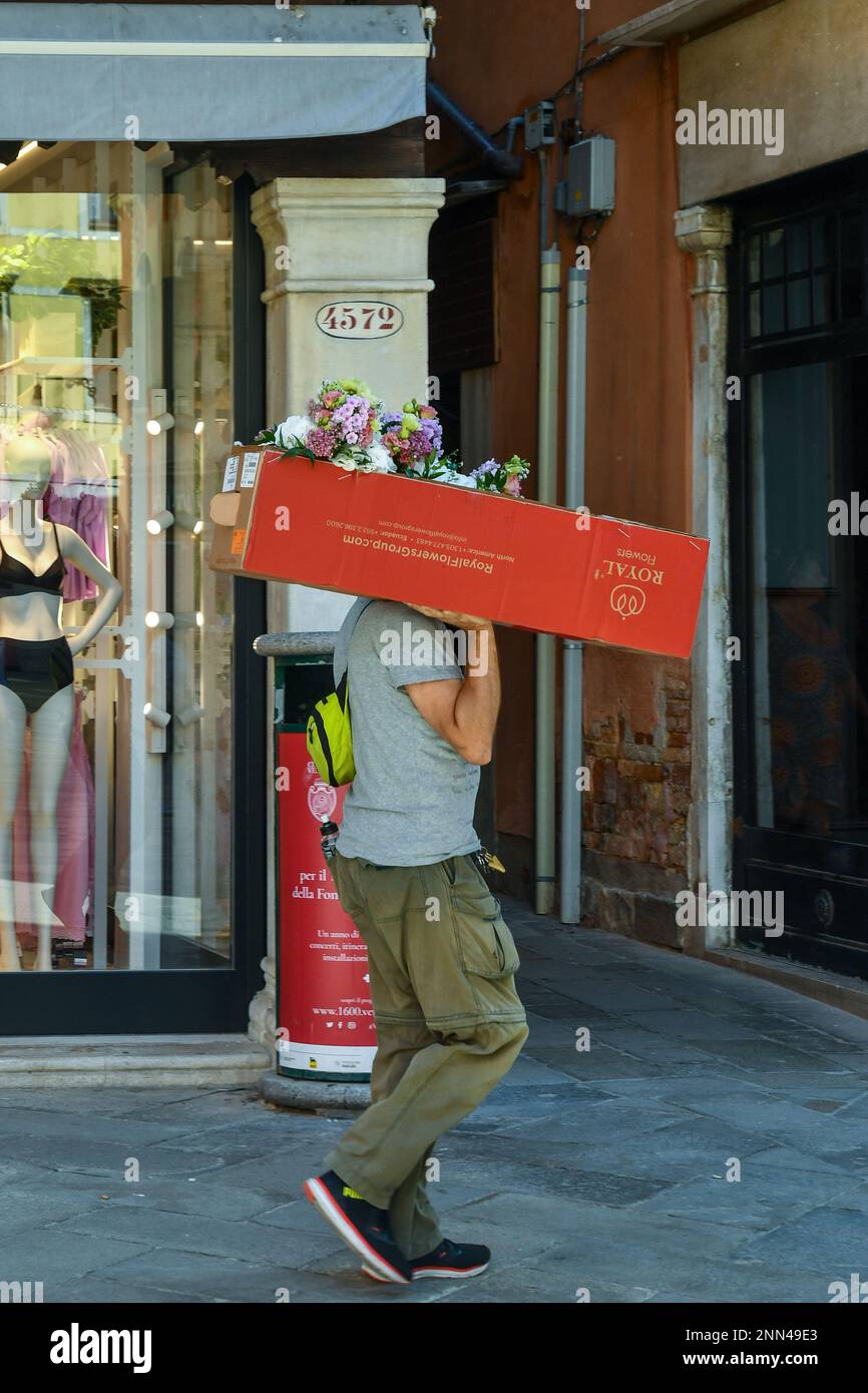 Venditore di fiori che trasporta bouquet freschi all'interno di una scatola in un vicolo ('calle') di Venezia, Veneto, Italia Foto Stock