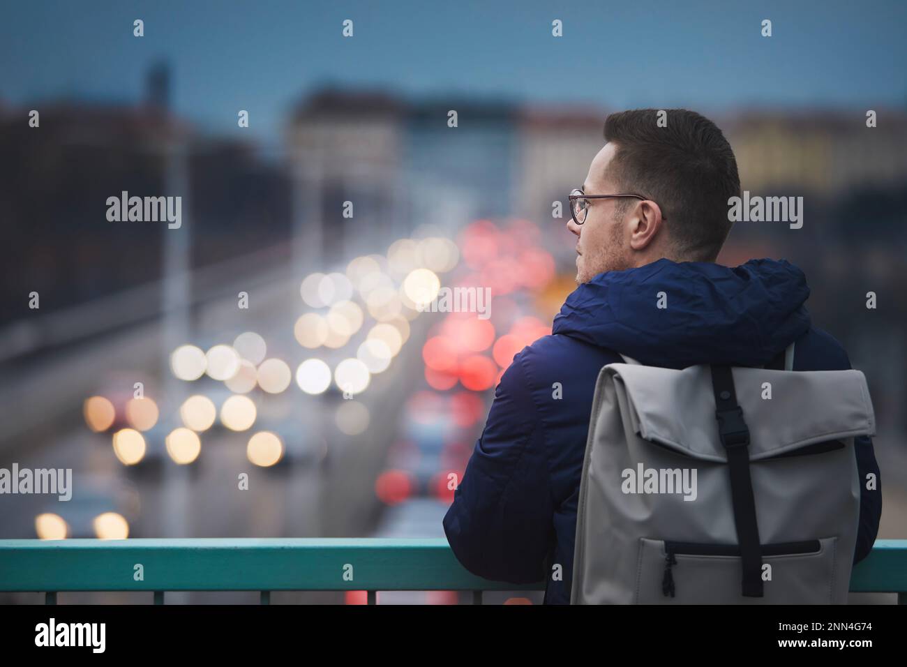 Uomo che guarda la strada trafficata della città. Ritratto contro scena urbana con auto al crepuscolo. Foto Stock