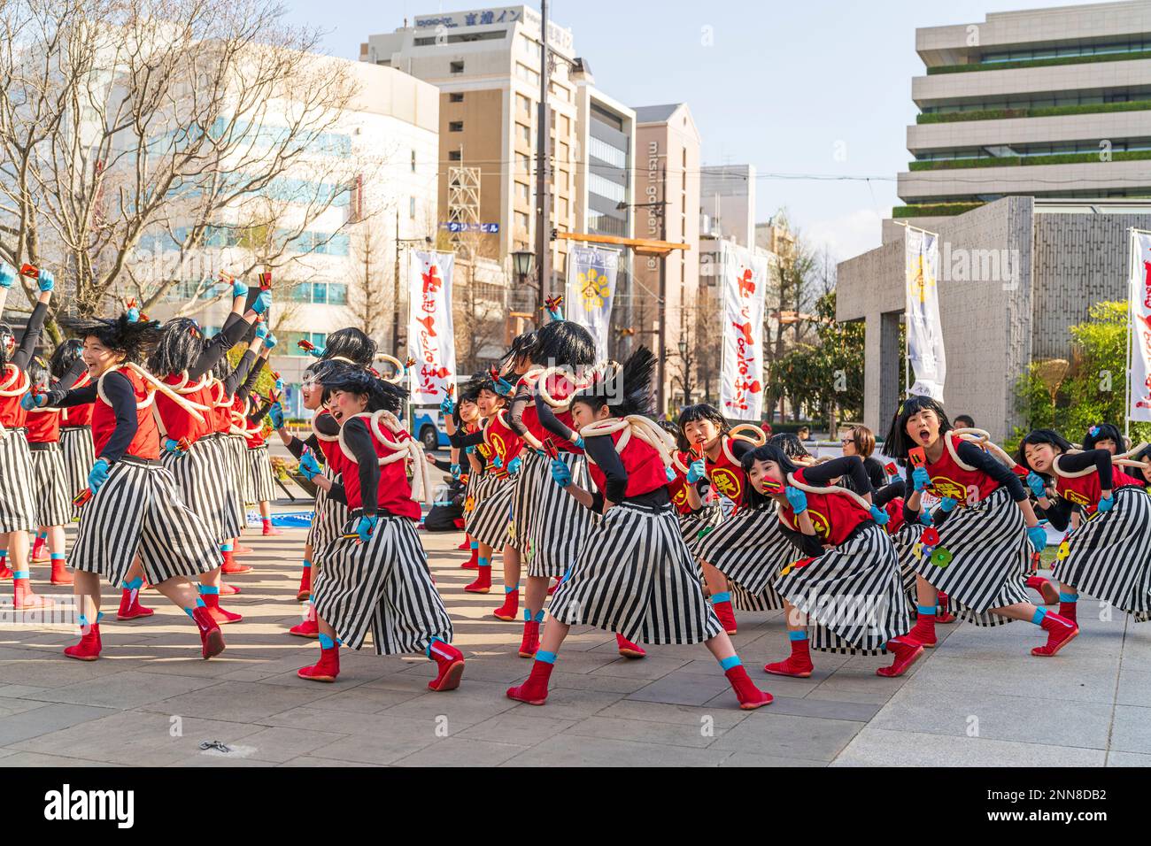 Squadra giapponese di danzatrici Yosakoi bambina che ballano e tengono naruko nella piazza pubblica della città durante l'annuale festival Kyusyu Gassai a Kumamoto. Foto Stock