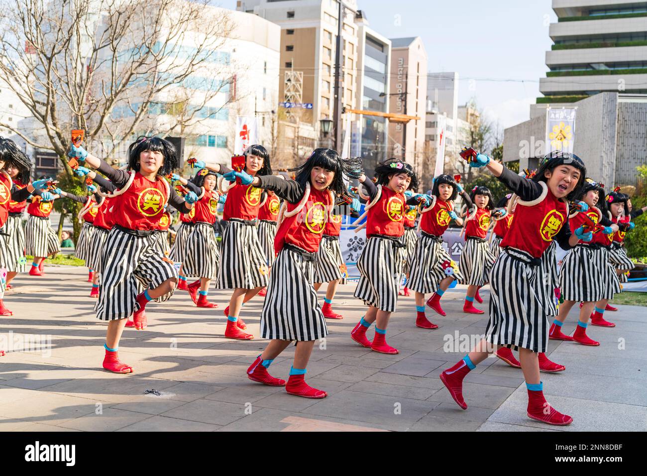 Squadra giapponese di danzatrici Yosakoi bambina che ballano e tengono naruko, clapper, nella piazza della città in occasione dell'annuale festival Kyusyu Gassai a Kumamoto. Foto Stock