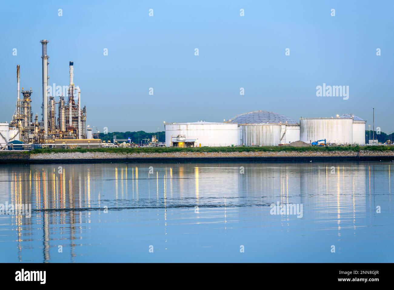 Serbatoi e torri di distillazione in una raffineria di petrolio su un porto al crepuscolo Foto Stock
