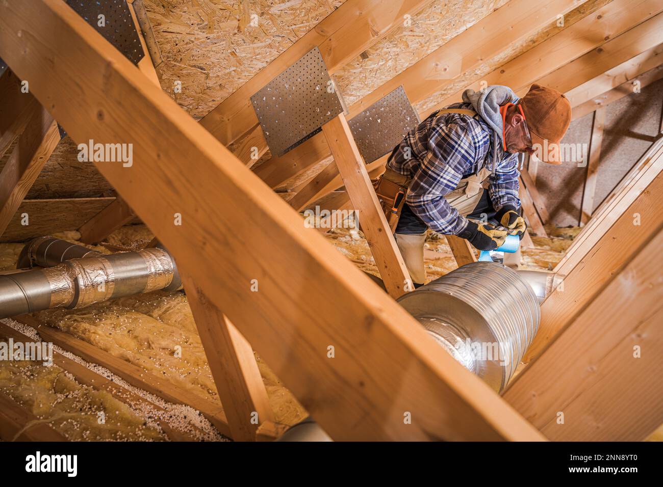 Tecnico HVAC professionista che esegue l'installazione del filtro del condotto dell'aria nella sezione soffitta dell'edificio residenziale. Foto Stock