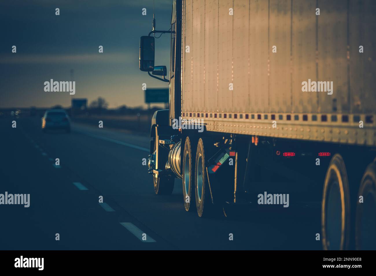 Vista posteriore primo piano di American semi-camion sulla strada che guida in avanti in Sunset Rays. Tema del trasporto. Foto Stock
