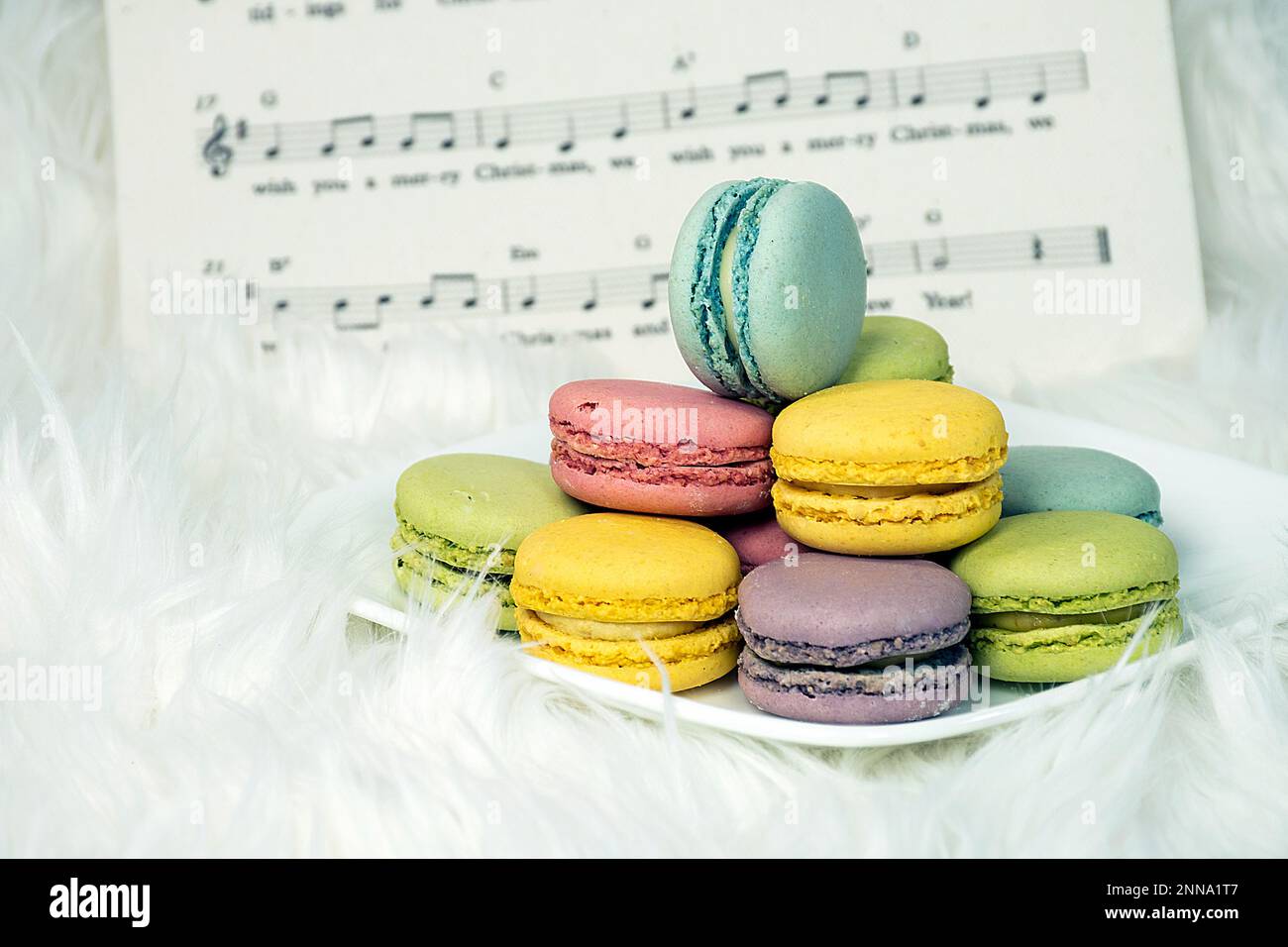 Macaron colorati su piatto quadrato bianco e pelliccia soffice con sottofondo di musica natalizia Foto Stock