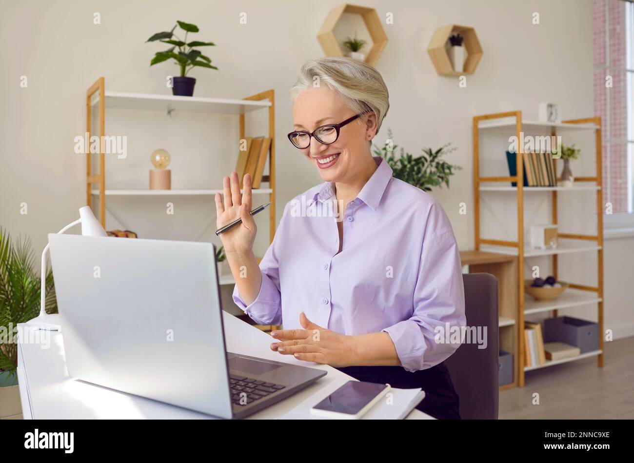 Una donna anziana dai capelli grigi con un sorriso sul viso usa un notebook per comunicare. Foto Stock
