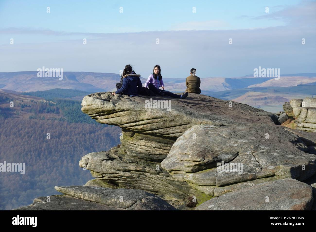 Persone sedute su una parete rocciosa a Bamford Edge, Hope Valley Foto Stock