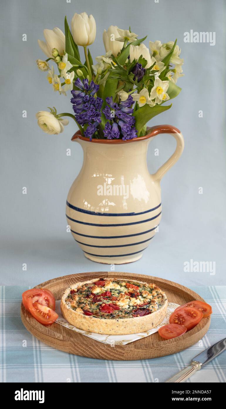 Peperone rosso e quiche di verdure su un piatto accanto a una brocca di fiori freschi di primavera Foto Stock