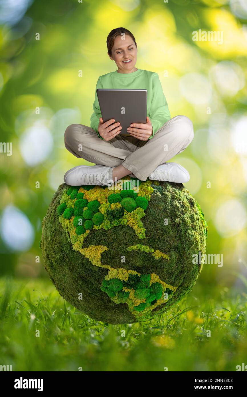Donna con tablet digitale seduto sul pianeta verde Terra. Concetto di sviluppo sostenibile e di educazione ambientale Foto Stock