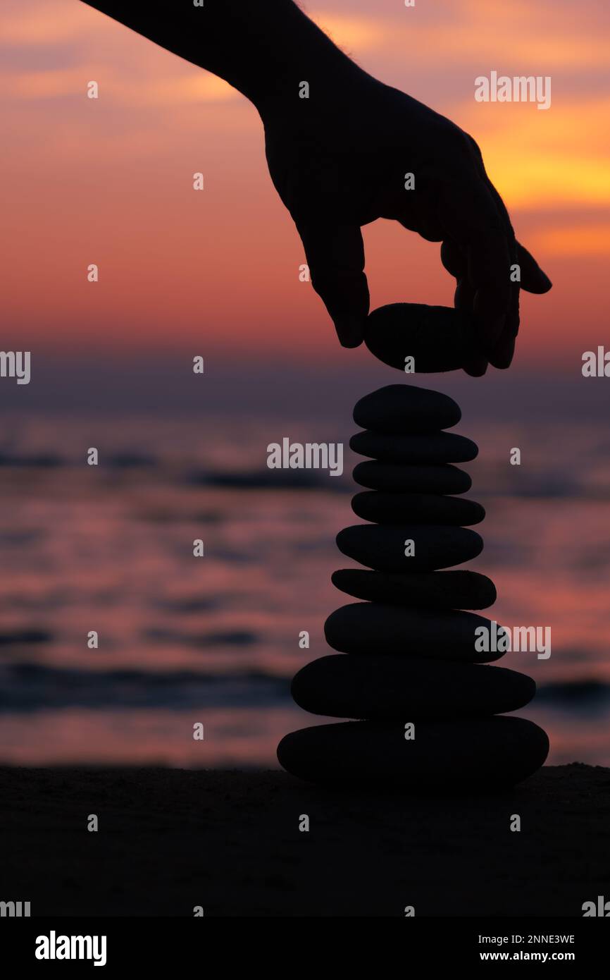 İmage verticale, profilo equilibrato piramidale di ciottoli sulla spiaggia al tramonto. Pietre Zen sulla spiaggia di mare, meditazione, spa, armonia, calma, equilibrio. Foto Stock