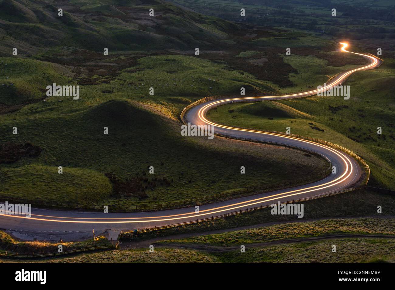 Tortuosa strada rurale curvilinea con sentiero leggero dai fari che conduce attraverso la campagna britannica. Foto Stock