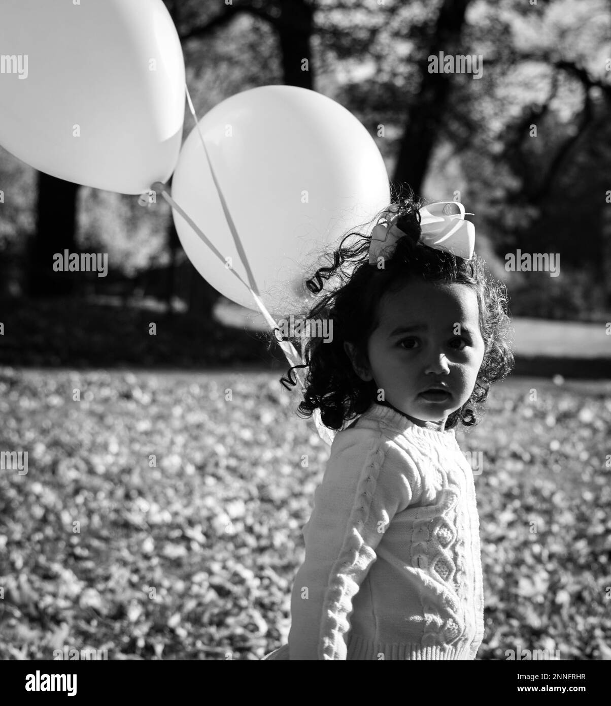 Piccola bambina bionda di due anni con grandi palloncini rosa e bianchi per  la sua festa di compleanno.