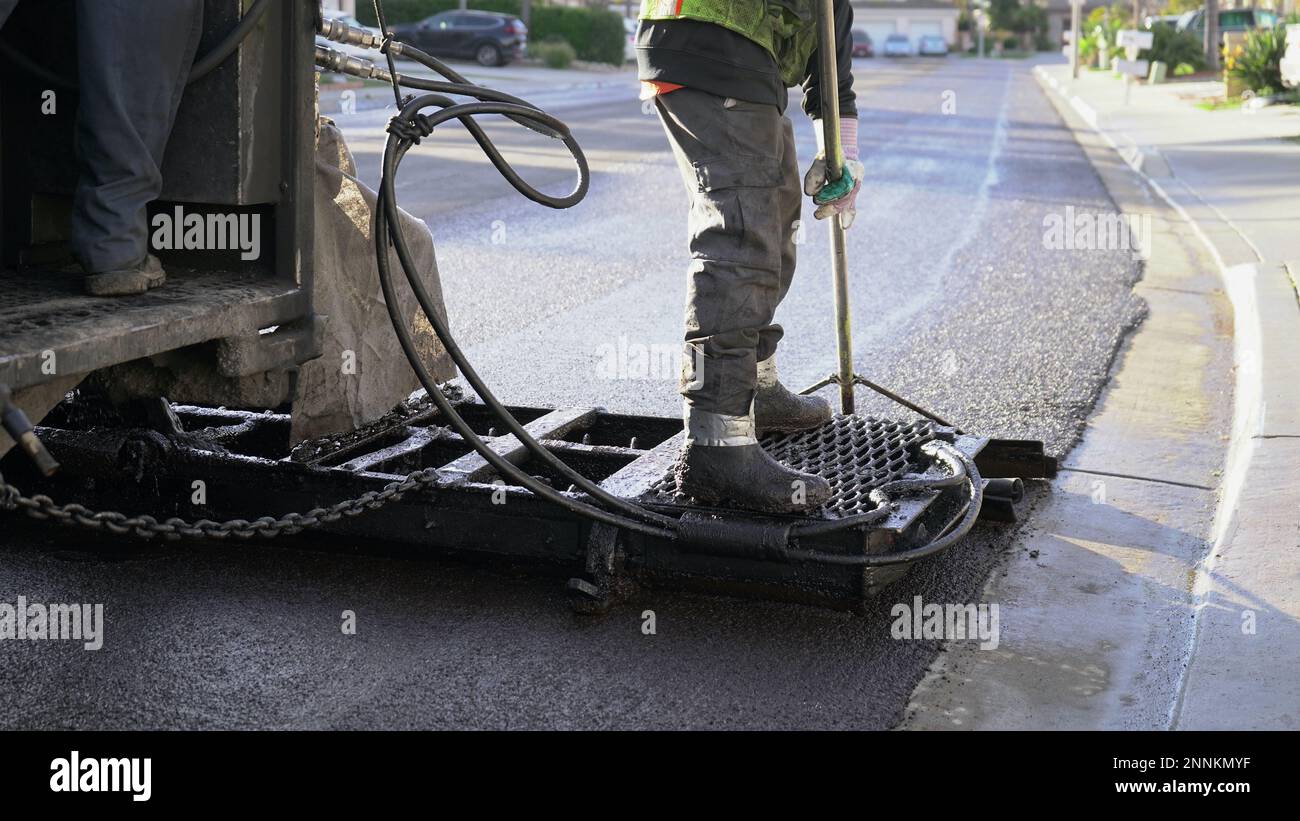 L'operatore che indossa stivali e indumenti protettivi si sposta sulla macchina per levigare la guarnizione in pasta fresca durante l'applicazione Foto Stock