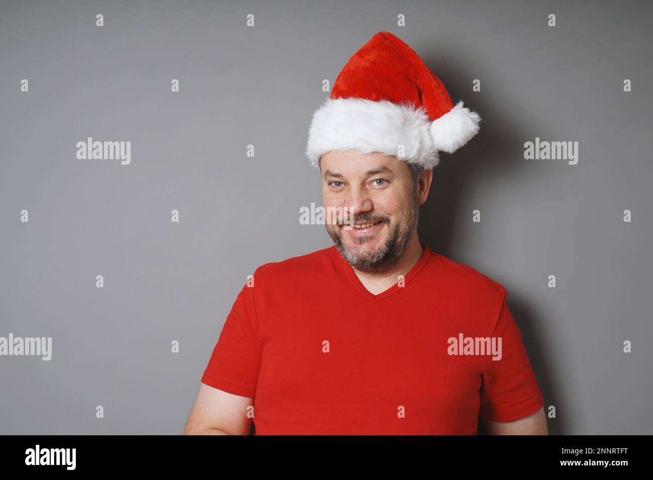 Sorridente uomo di mezza età con barba ingrigimento indossando santa hat e t-shirt rossa - la gente reale concetto di natale Foto Stock