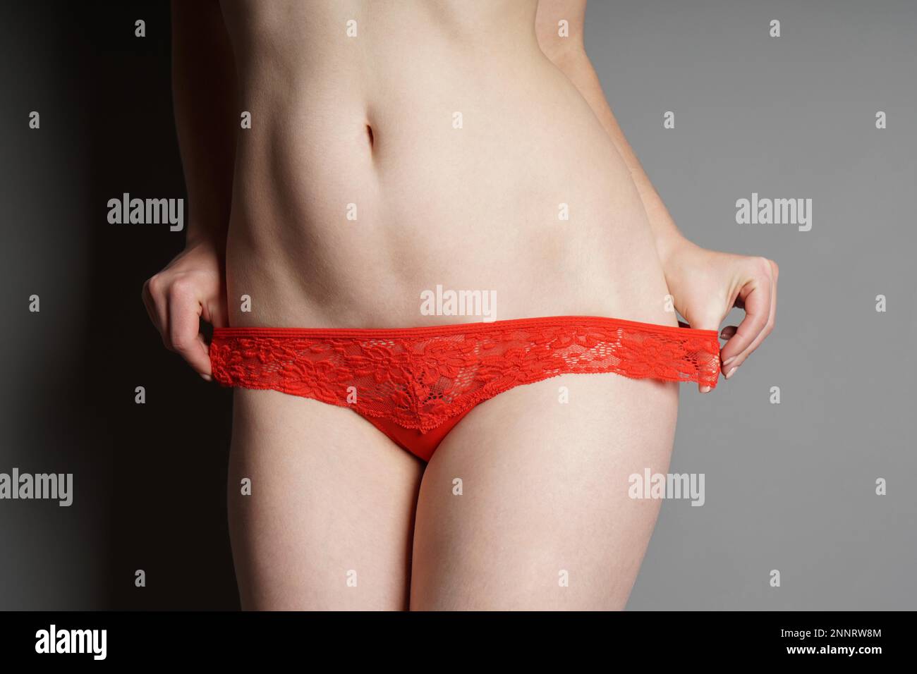 ragazza irriconoscibile che tira giù le mutandine rosse del pizzo - il concetto di striptease o di seduzione Foto Stock