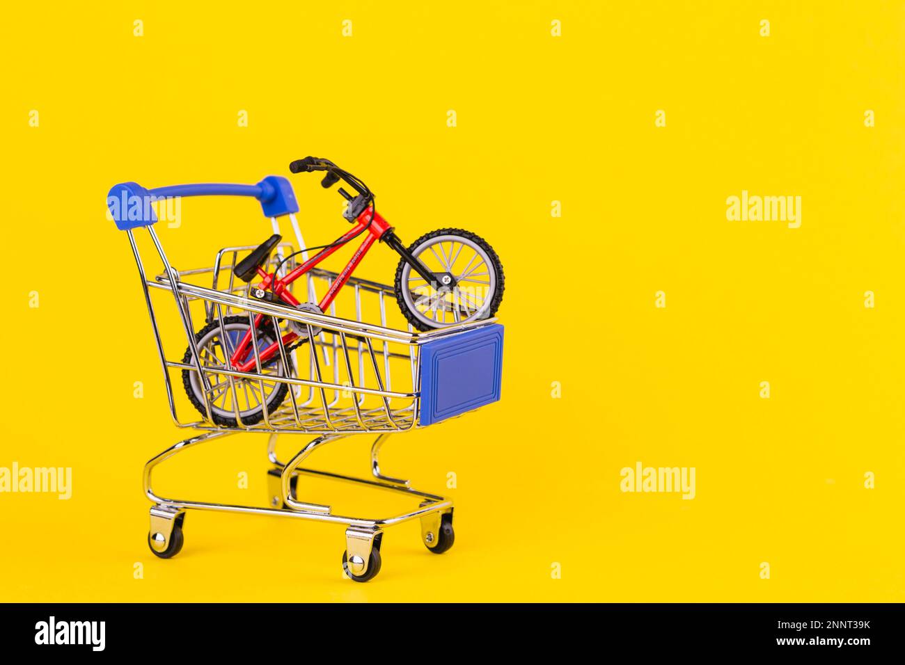 Piccolo carrello di shopping giocattolo per biciclette su sfondo giallo Foto Stock