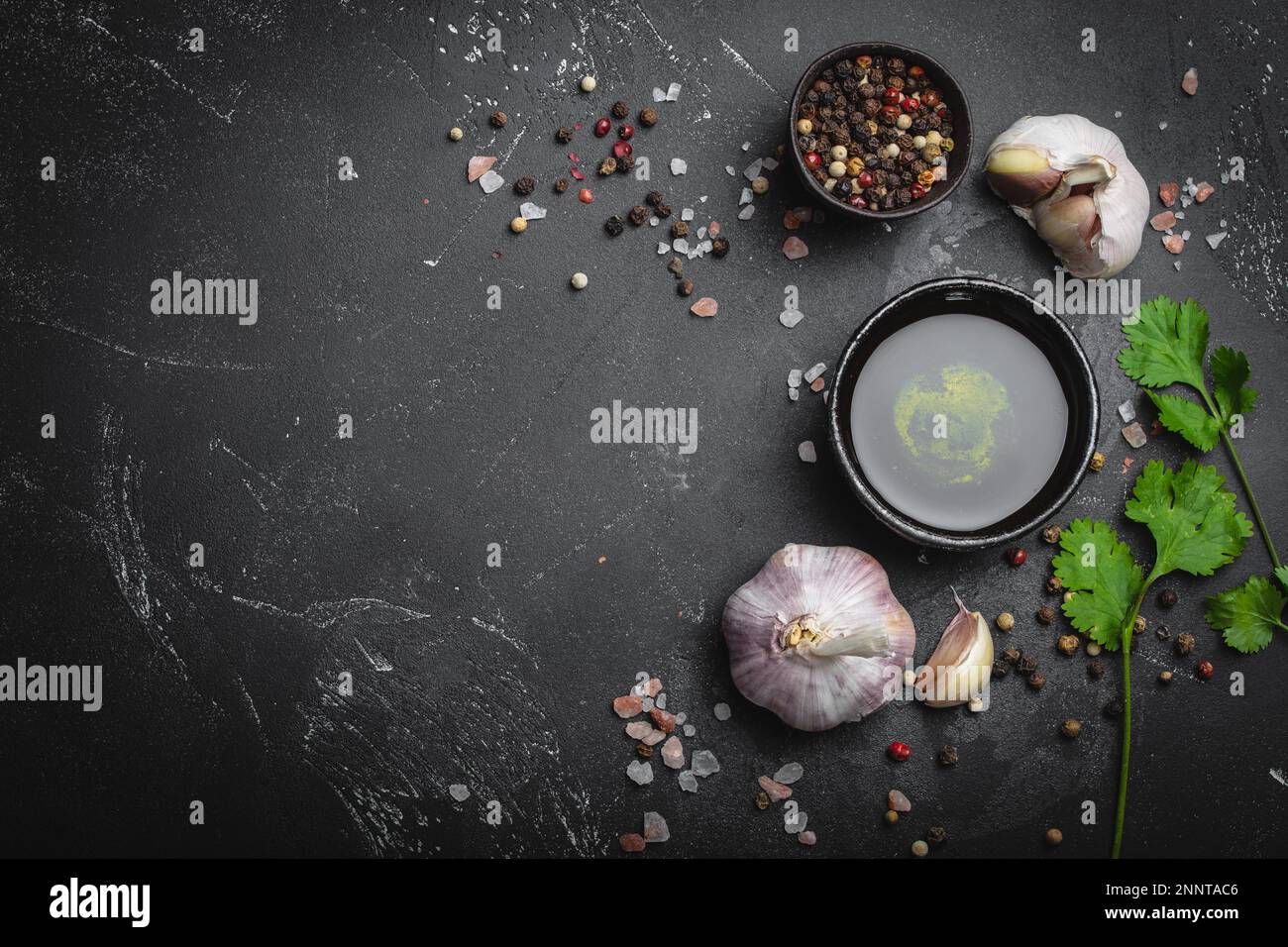 Primo piano degli ingredienti della cucina tradizionale: Aglio, olio d'oliva, sale, pepe, erbe fresche su fondo rustico scuro. Struttura per alimenti, concetto per la cottura Foto Stock