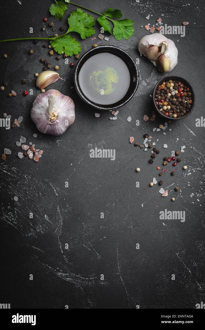 Primo piano degli ingredienti della cucina tradizionale: Aglio, olio d'oliva, sale, pepe, erbe fresche su fondo rustico scuro. Struttura per alimenti, concetto per la cottura Foto Stock