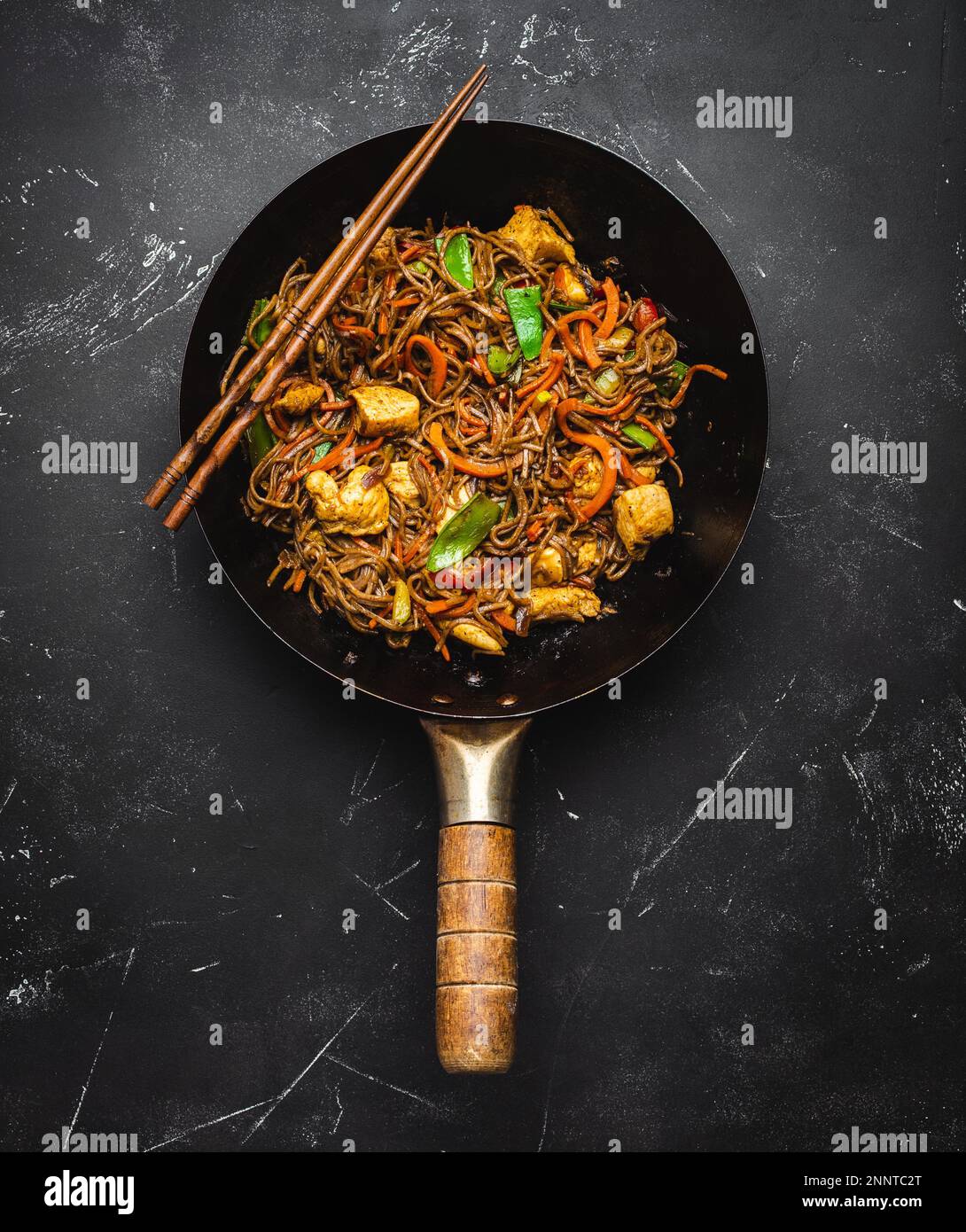 Mescolare gli spaghetti di soba con il pollo, le verdure nella vecchia  teglia rustica del wok, le bacchette su fondo di pietra nera, primo piano,  vista dall'alto. Tradizionale Foto stock - Alamy