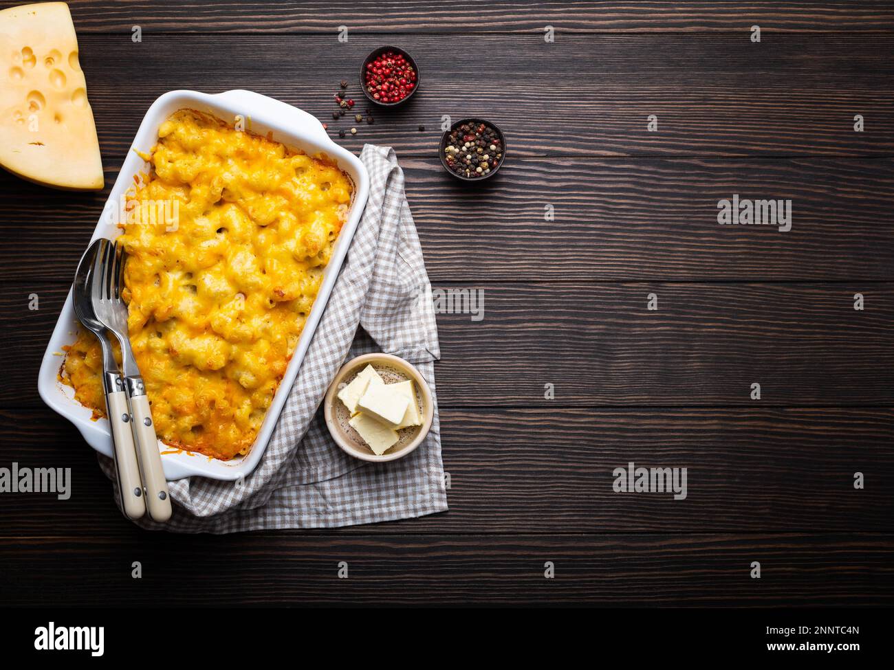 Primo piano di maccheroni al forno e formaggio in casseruola bianca su fondo ligneo, con condimenti, burro, cucchiaio e forchetta, vista dall'alto, spazio per il testo. Foto Stock