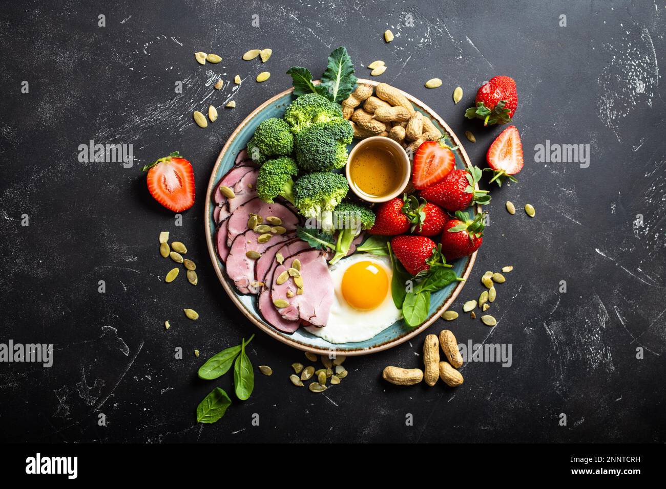 Ketogenic basso concetto di dieta dei carbs, vista dall'alto. Piatto su fondo nero di pietra con cibi keto: Uova, carne, olio d'oliva, broccoli, bacche, noci, semi Foto Stock