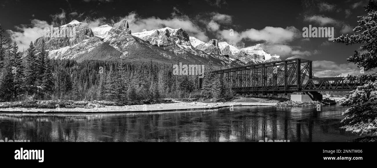 Ponte ferroviario sul fiume Bow nel paesaggio di montagna coperto di neve in bianco e nero, Alberta, Canada Foto Stock