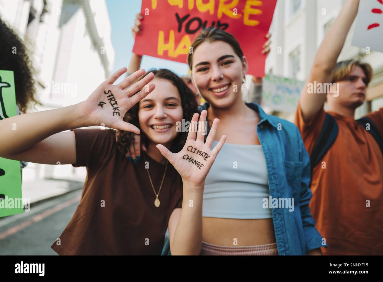 Sciopero Gen Z per il cambiamento climatico. Ragazze adolescenti felici sorridenti alla macchina fotografica mentre marciano contro il riscaldamento globale con un gruppo di manifestanti. Atto giovanile Foto Stock