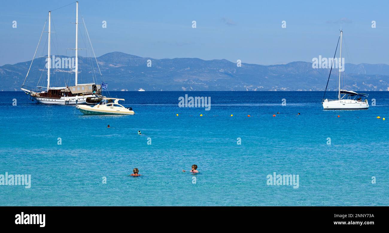 Turisti in spiaggia e barche a vela a Lakka Bay, Paxos, Isole IONIE, Grecia Foto Stock