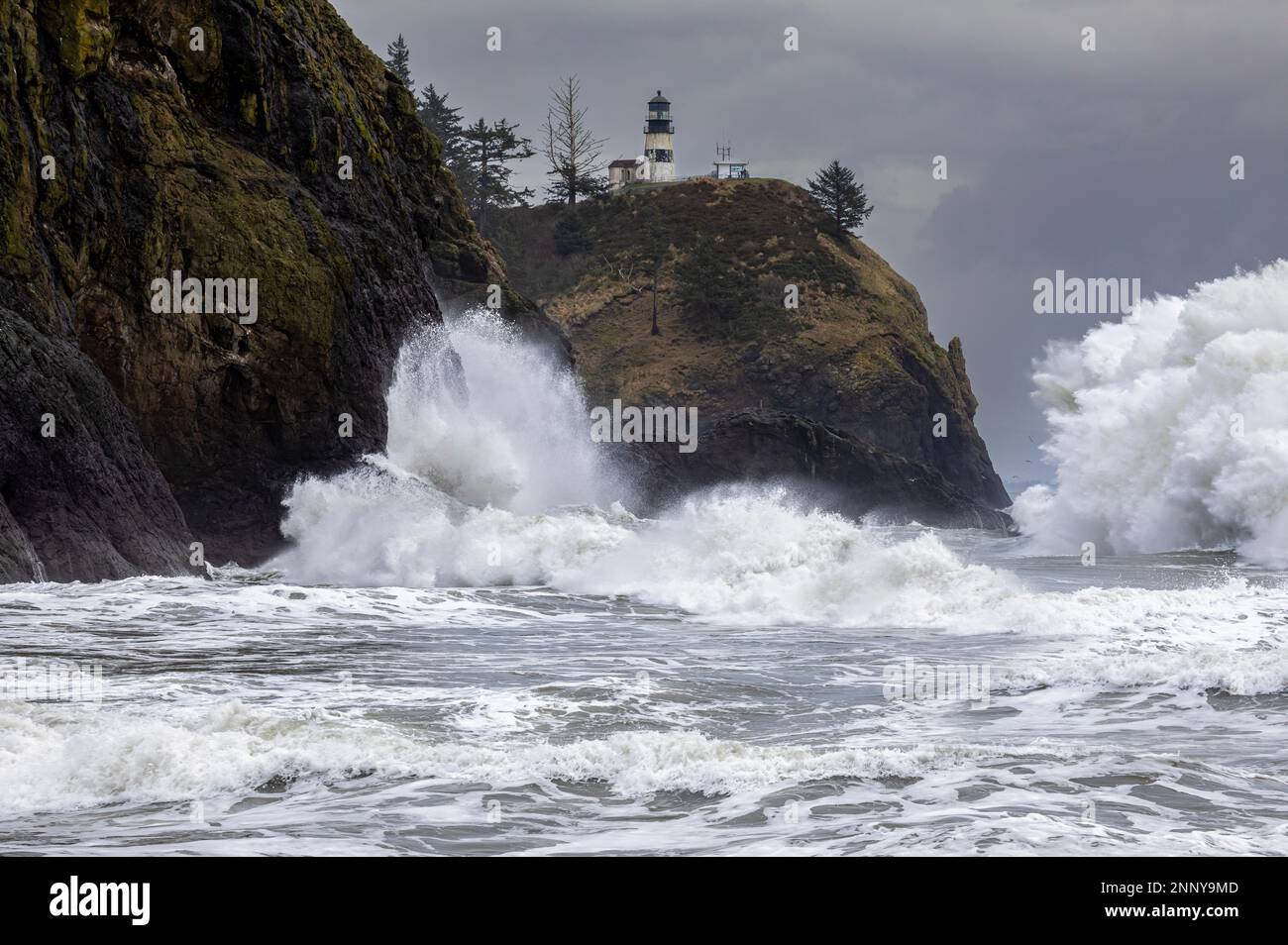 WA23076-00...WASHINGTON - onda che spruzzi contro le scogliere sotto Cape delusione Faro e gigante onda di splash posteriore da onda uscente colpire Foto Stock