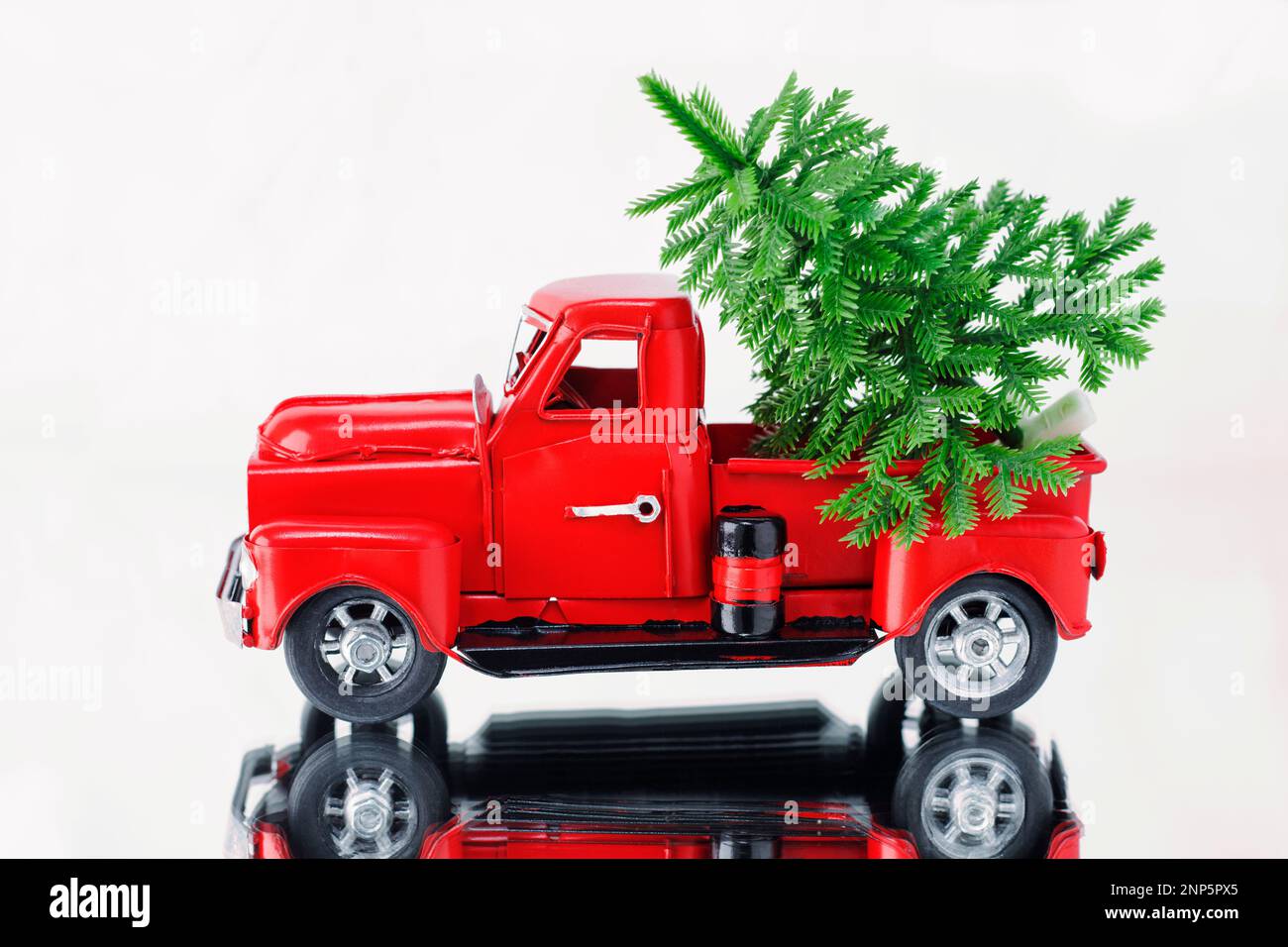 Albero di Natale in un camion di Natale rosso su uno sfondo bianco, riflesso in una superficie di specchio. Concept - biglietto di auguri per Natale e Capodanno, holi Foto Stock