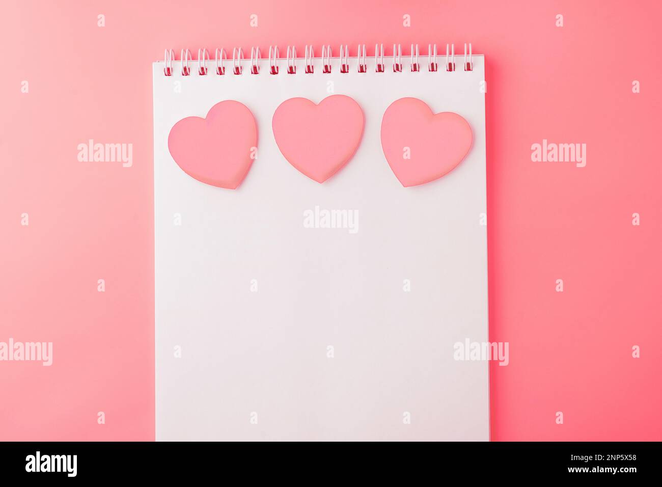 San Valentino sfondo. Apri il notebook vuoto e i cuori rosa su uno sfondo rosa pesca. Scrivere lettere romantiche. Vista dall'alto. Spazio di copia Foto Stock