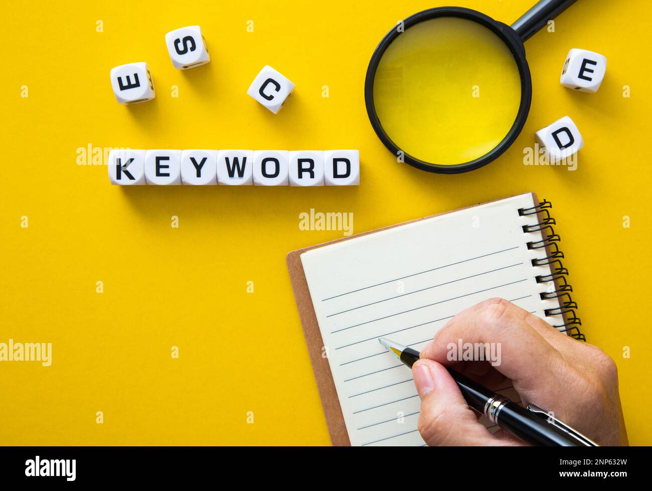 Mano che scrive appunti per la ricerca di parole chiave, circondata da blocchi di lettere e una lente d'ingrandimento Foto Stock