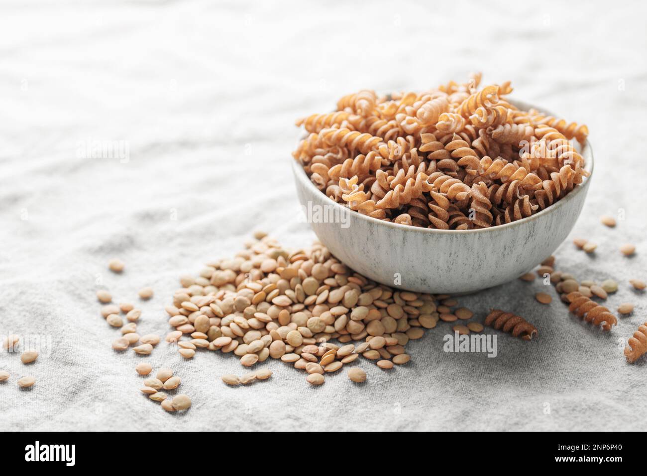 Lenticchie verdi fusilli su fondo tessile grigio. Una ciotola di pasta cruda e lenticchie verdi. Pasta senza glutine. Foto Stock