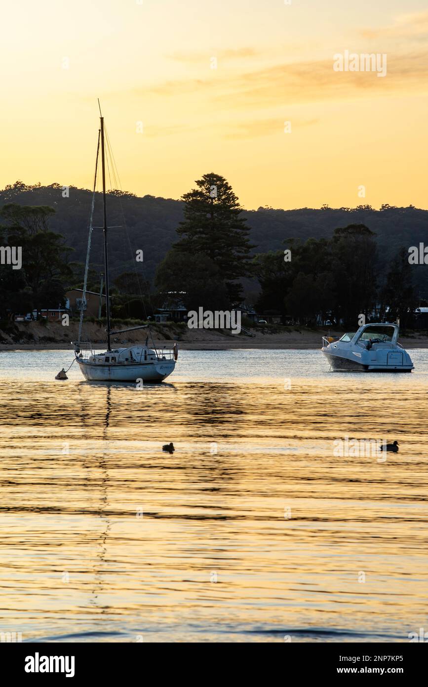 Le barche si sono legate al loro ormeggio durante l'ora d'oro nella calda luce del crepuscolo a Ettalong Beach sulla costa centrale del New South Wales in Australia Foto Stock