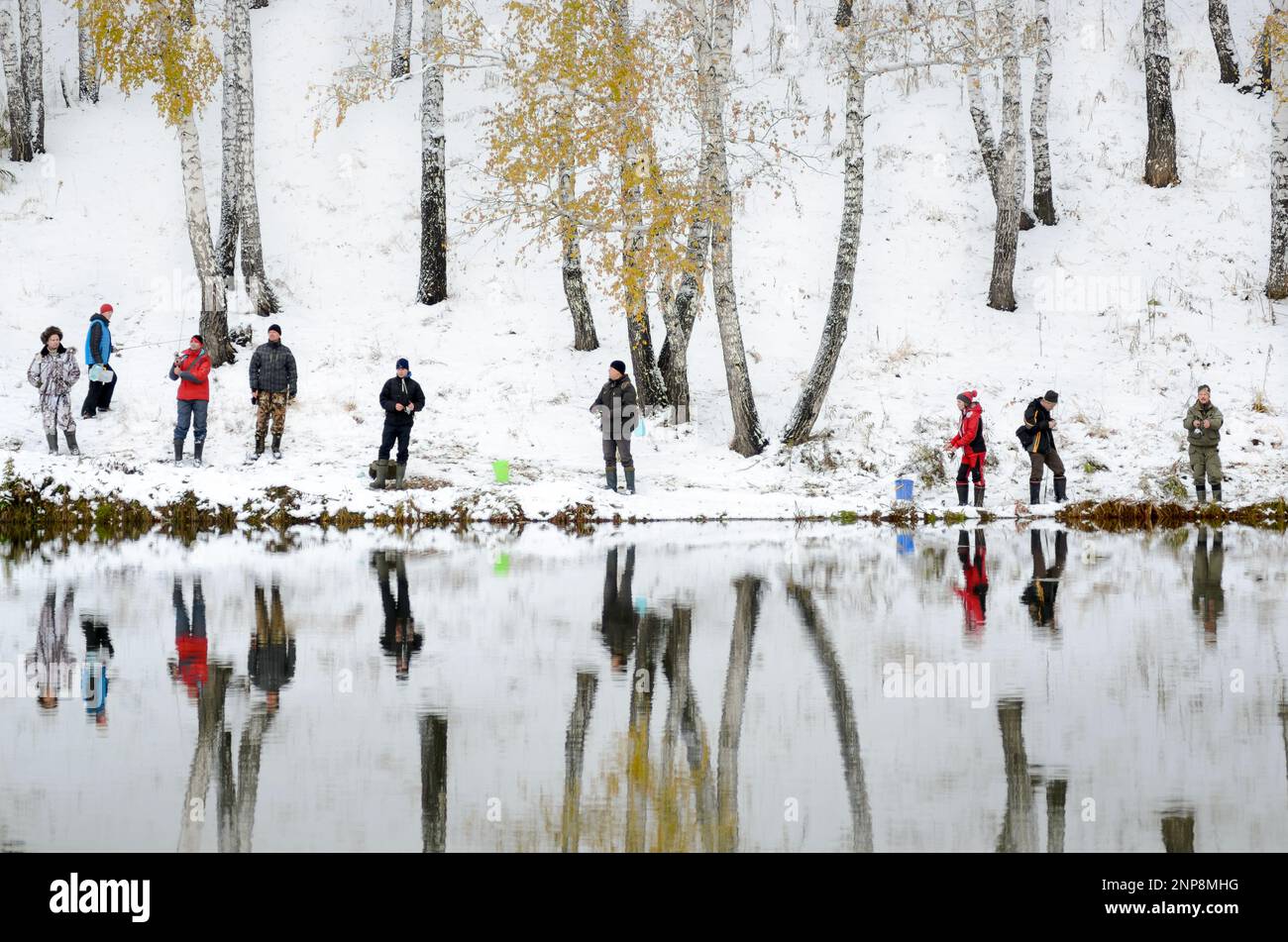 Le persone sono pescatori su entrambe le rive innevate del lago alla concorrenza in Russia nella foresta Foto Stock