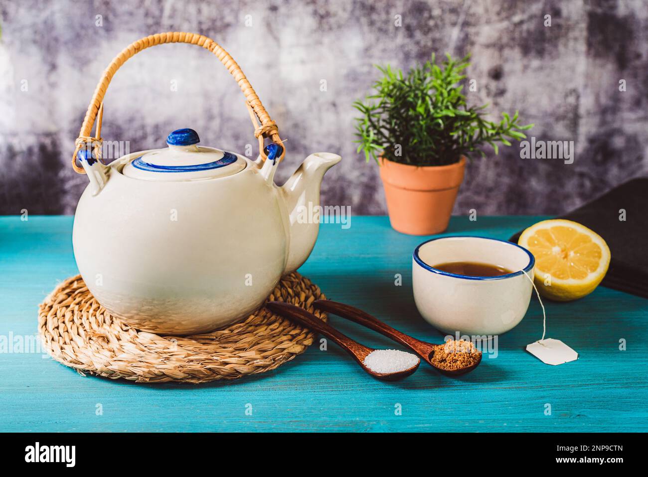 Teiera in porcellana accanto ad una tazza di tè e mezzo limone, con due cucchiai di legno, uno con zucchero bianco e l'altro con zucchero di canna. Foto Stock