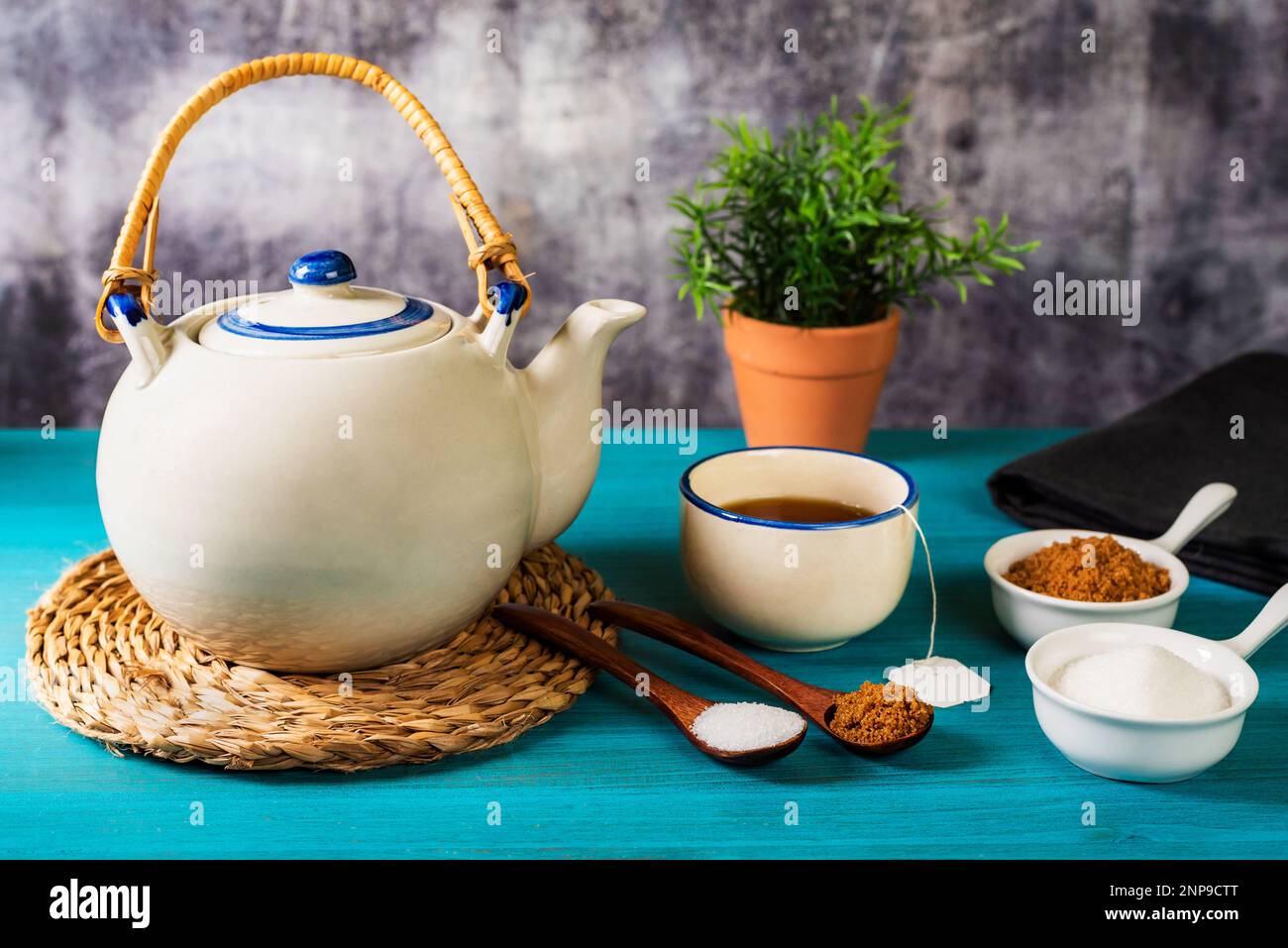 Teiera in porcellana accanto ad una tazza da tè, con due cucchiai di legno, uno con lo zucchero bianco e l'altro con lo zucchero di canna, e due piccoli contenitori con entrambi i Ty Foto Stock