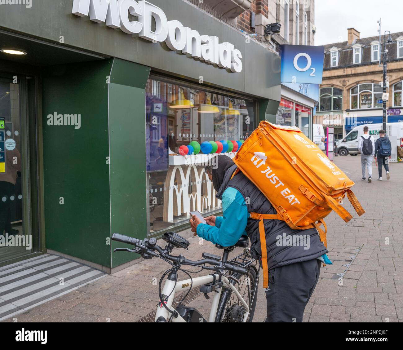 Un ciclista di consegna del pasto giusto aspetta fuori un McDonald's. Foto Stock