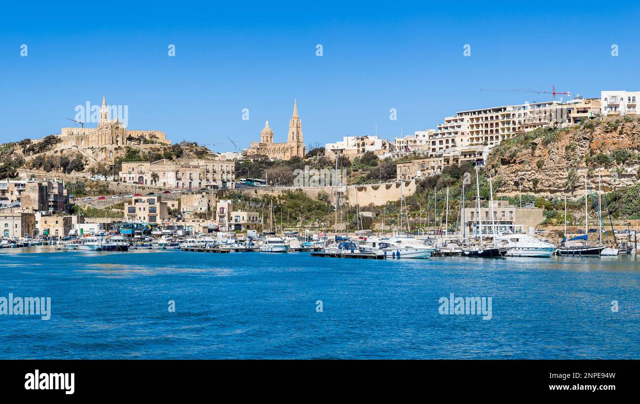 Porto di Mgarr e porticciolo visto in una giornata di sole sotto un cielo blu mentre la nostra barca si avvicina all'isola di Gozo. Foto Stock