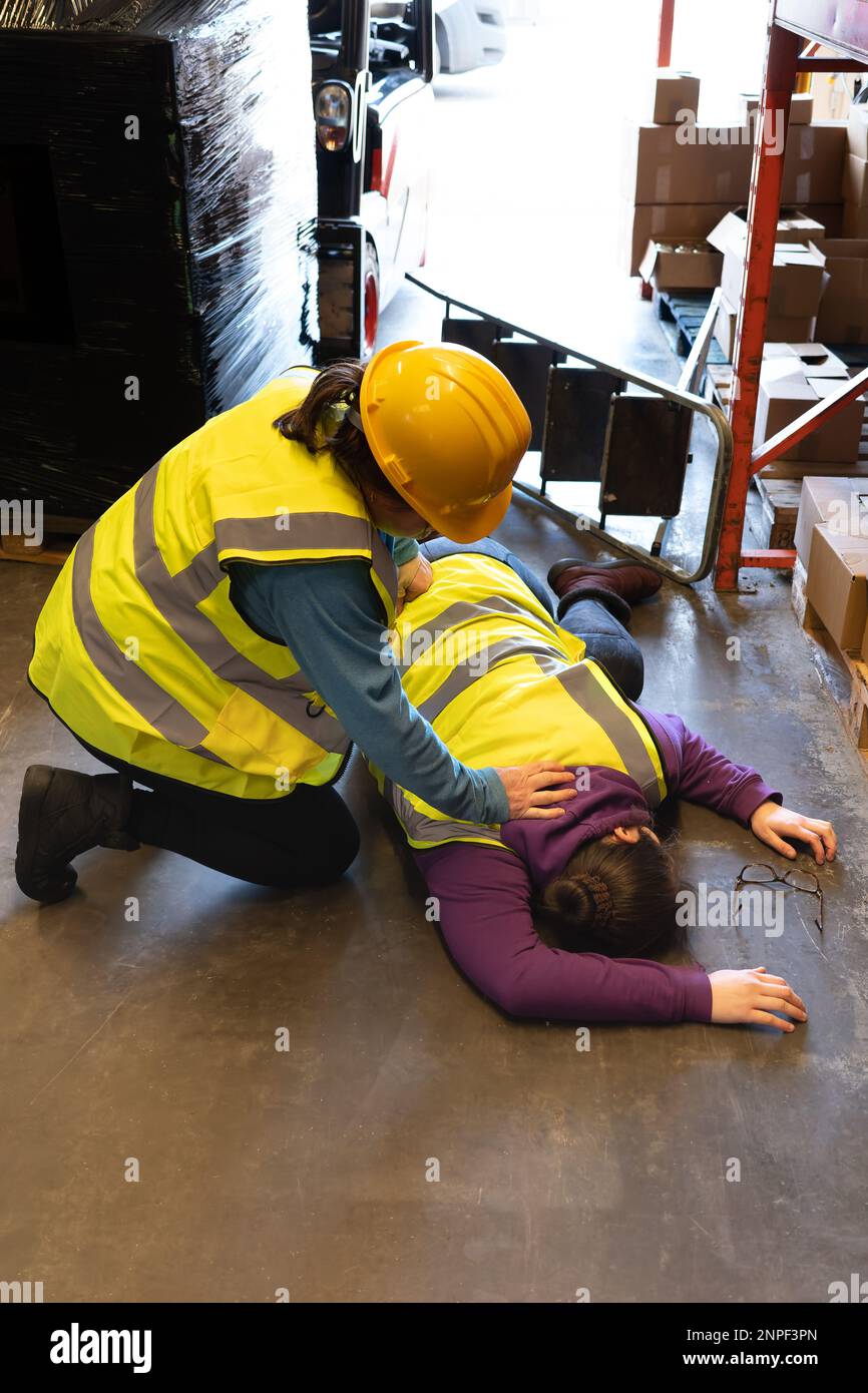 Incidente sul posto di lavoro, la giovane donna si trova ferita dopo la caduta dalla scala a gradini i membri del secondo personale tendono alla persona Foto Stock
