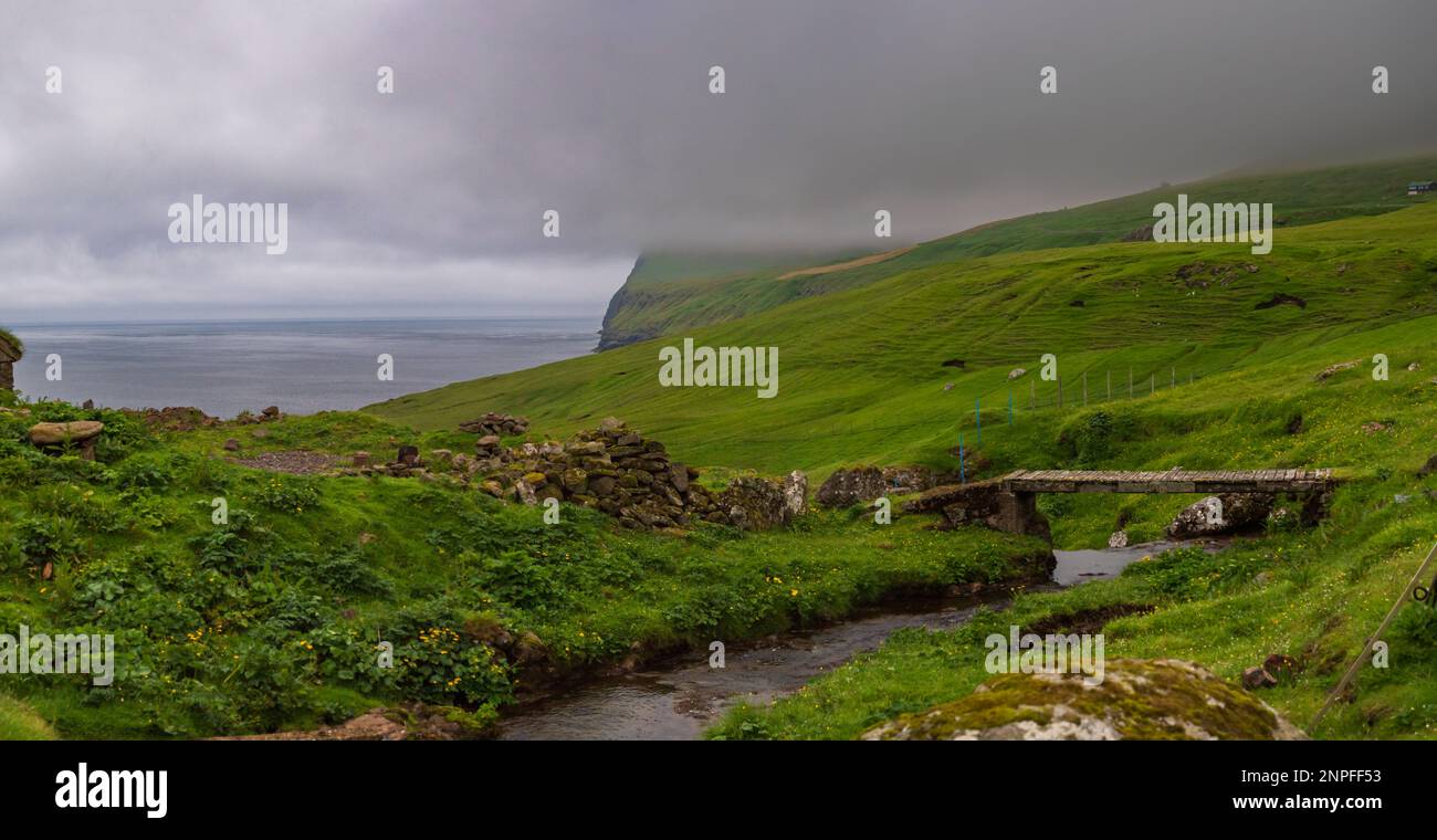Vista sull'Oceano Atlantico e sulle colline ricoperte di nuvole dal piccolo villaggio di Norðradalur in una giornata di nebbia, Streymoy, Isole Faroe, Regno di Danimarca. N. Foto Stock