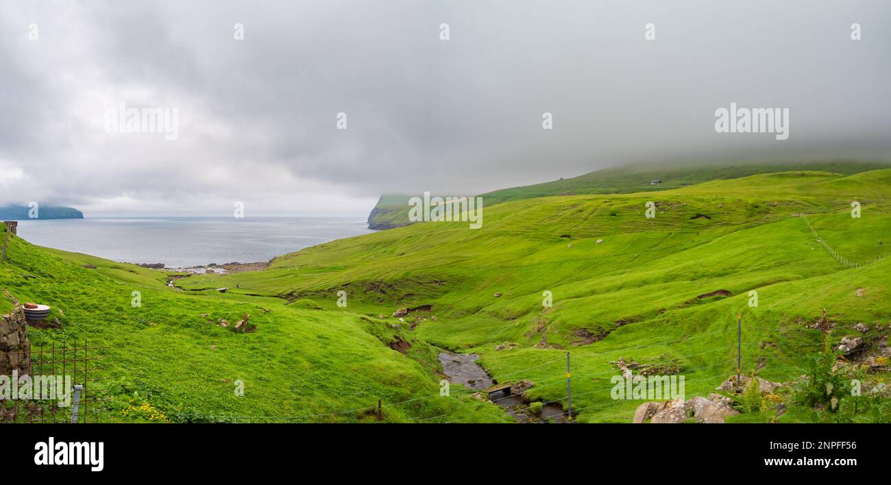 Vista sull'Oceano Atlantico e sulle colline ricoperte di nuvole dal piccolo villaggio di Norðradalur in una giornata di nebbia, Streymoy, Isole Faroe, Regno di Danimarca. N. Foto Stock