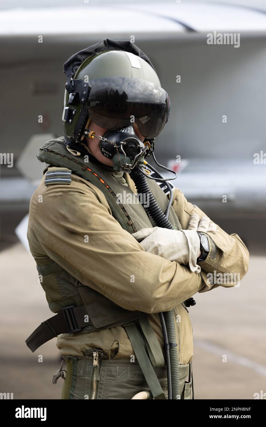 Military Fighter Pilot con casco, visiera e maschera di ossigeno in tuta volante con jet da combattimento sullo sfondo. Posa della pistola superiore per il pilota da combattimento Foto Stock