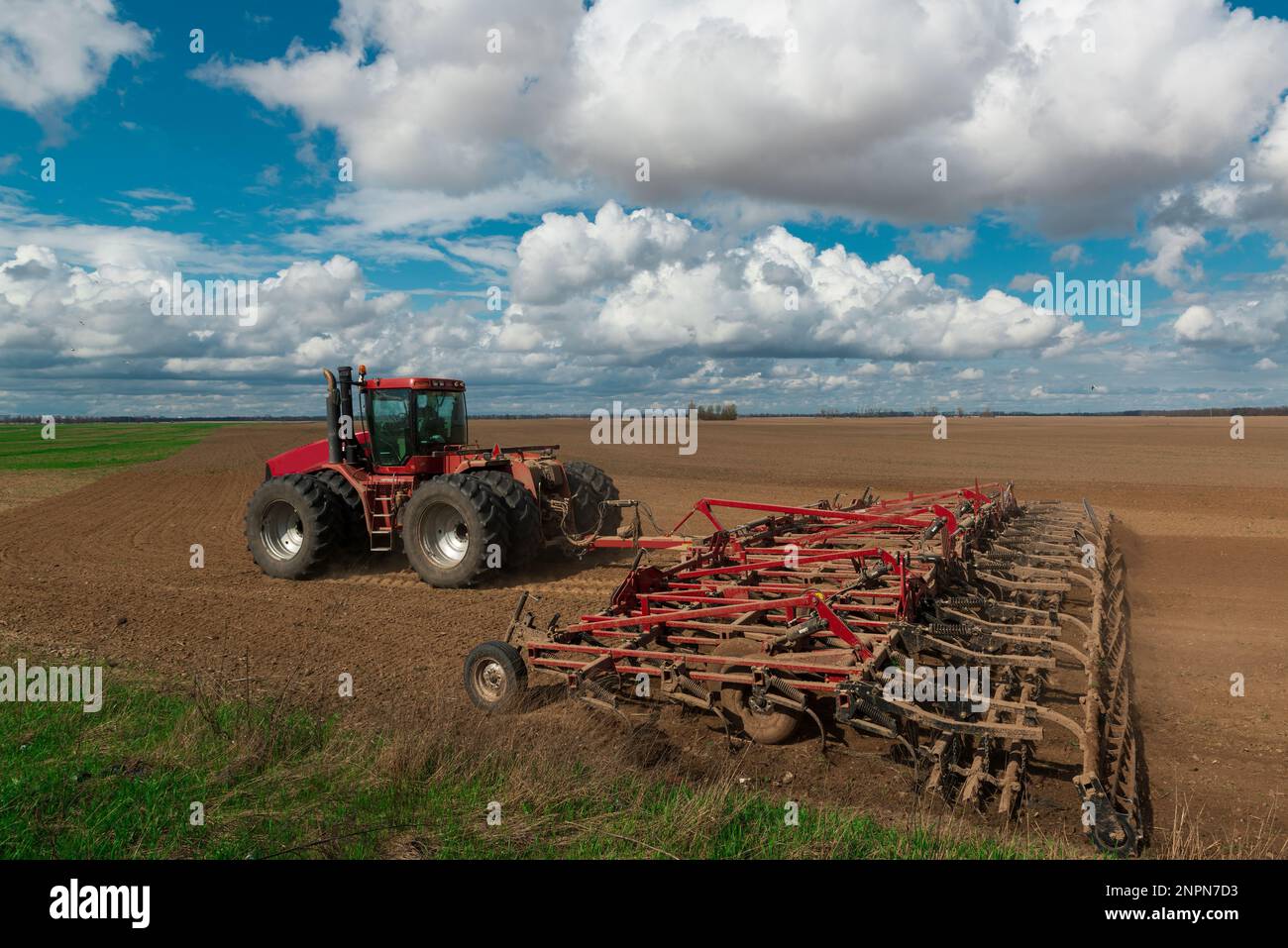 Il trattore rosso aratri il campo agricolo. Lavori agricoli primaverili in Ucraina. Terreno coltivato e cielo con nuvole. Paesaggio di campagna Foto Stock