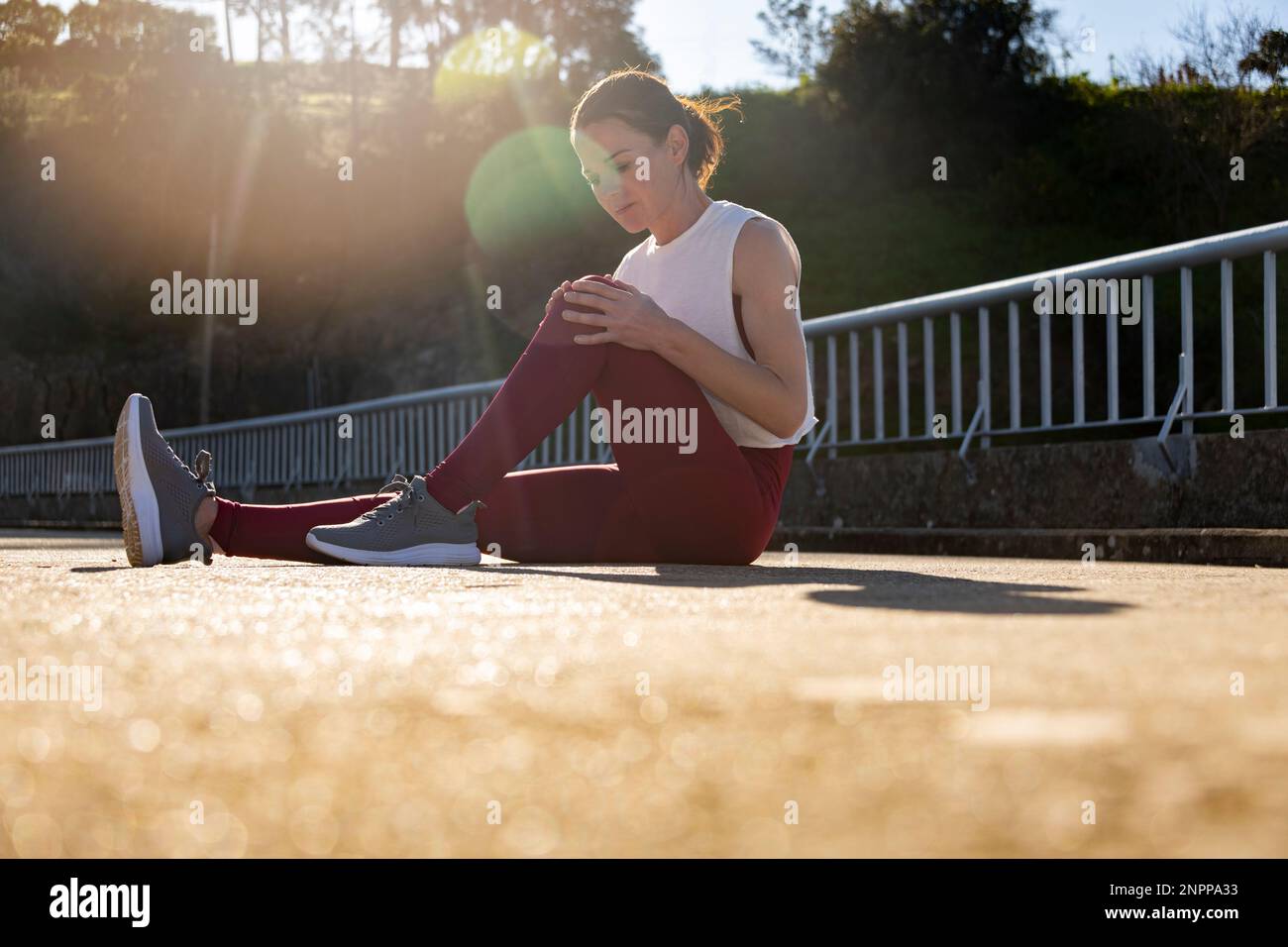 Donna runner seduto sulla strada tenendo il ginocchio, lesioni sportive Foto Stock