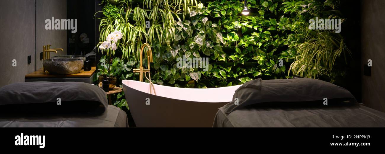 Bagno in moderno salone di bellezza, lussuoso bagno interno in spa con giardino verticale. Parete di piante verdi, lettini da massaggio e vasca da bagno in hotel. Concetto di na Foto Stock