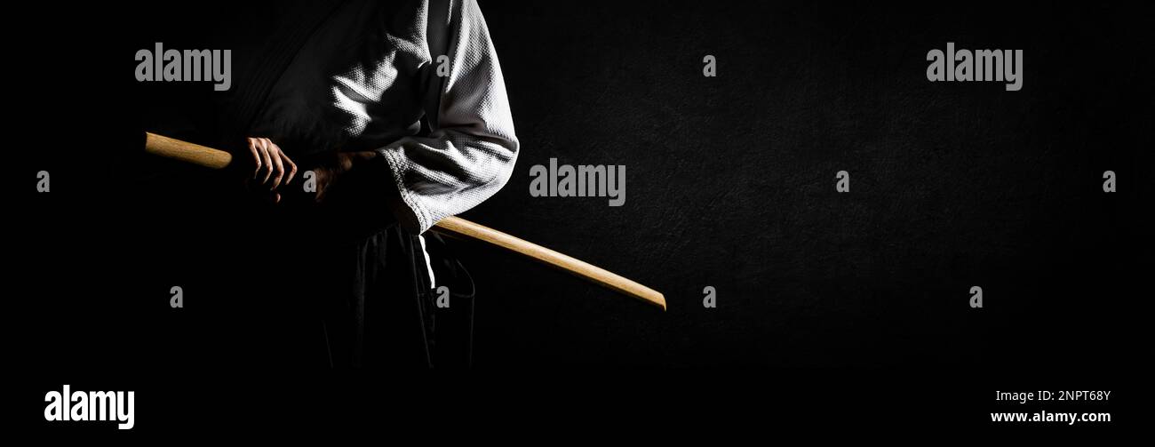 Una persona in hakama nero in piedi in posa di combattimento con la spada di legno bokken su grunge sfondo scuro banner. Profondità di campo bassa. SDF. Foto Stock