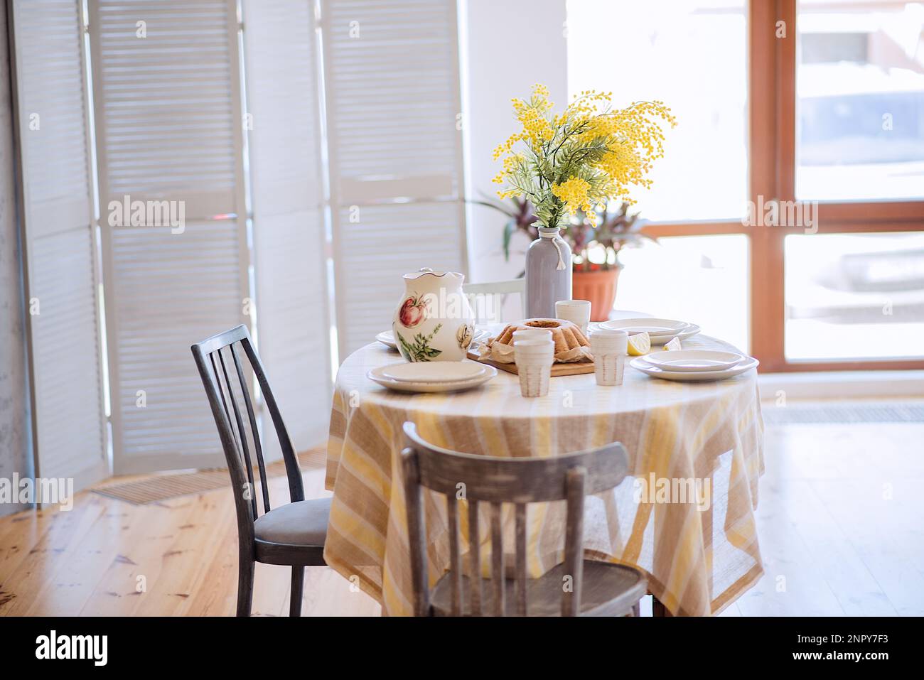 Primavera, Pasqua interni in stile scandinavo. Rustico soggiorno con un luminoso armadio, mimosa giallo in vaso. La tabella viene impostata in modo festivo con ceram Foto Stock